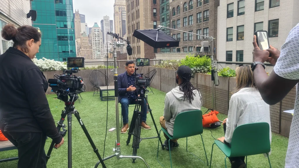 Behind the scenes of the outdoor interview, showing the battery-powered Flex Mat on a C-stand with a boom mic, all working to augment the natural sunlight.