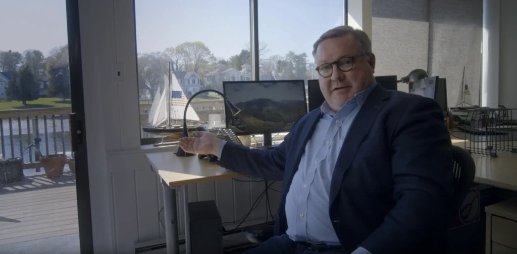A man in a suit and glasses is being interviewed in a well-lit office with a view of a harbor. This is an example of a solo storyteller interview lighting setup.